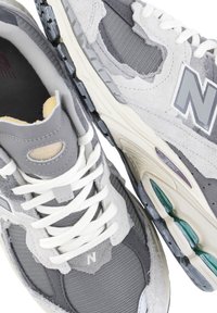 Le scarpe da ginnastica grigie presentano un mix di materiali in suede e mesh, lacci bianchi, un prominente logo "N" e una suola testurizzata con accenti color teal.