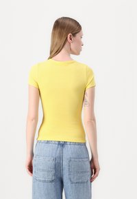 Haut jaune à rayures courtes avec un design ajusté. Le dos présente un col rond, associé à un jean taille haute bleu clair avec poches.