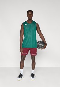 Green mesh sleeveless jersey with white accents, maroon athletic shorts with a striped design, black and white sneakers, and a basketball.