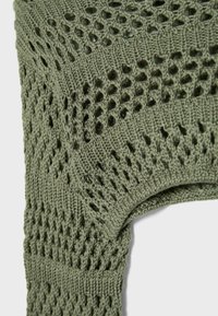 Tissu en maille avec motif dentelle ajourée en vert olive, montrant la texture détaillée et la courbe de l'emmanchure d'un vêtement.