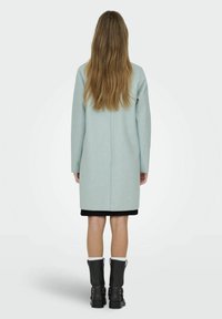 Cappotto in lana verde menta con maniche lunghe e vestibilità dritta, abbinato a stivaletti neri alla caviglia con un accento a fascia.