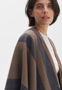 Brown and navy striped wool wrap with a loose, open design, featuring soft texture and draped fit. Suitable for layering over tops.