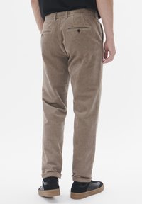 Beige corduroy pants with a straight-leg cut, textured fabric, and two back pockets. Styled with black sneakers and a tucked black shirt.