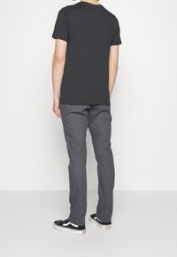 Czarna koszulka z krótkim rękawem, szare spodnie i czarne buty. Koszulka ma okrągły dekolt; spodnie mają prosty krój i gładką teksturę.