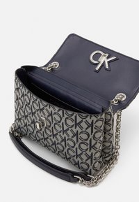 Borsa a tracolla Calvin Klein in tela blu navy e crema con un motivo logo. Presenta una tracolla in catena e pelle e dettagli metallici in argento.