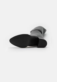 Bota negra hasta la rodilla con una superficie lisa y suave, punta redondeada, tacón grueso y una suela texturizada. Diseño sencillo sin adornos visibles.