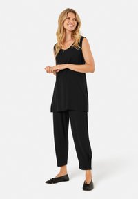 Zwarte mouwloze tuniek gecombineerd met zwarte tapered broeken en zwarte flats. Glad materiaal met een losse pasvorm en subtiele zijsplitsen.
