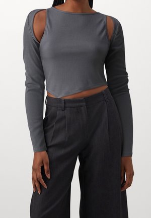 Grå ribbet crop top med lange ærmer og udskæring ved skuldrene, kombineret med mørke bukser med høj talje, skræddersyet pasform og sidelommer.