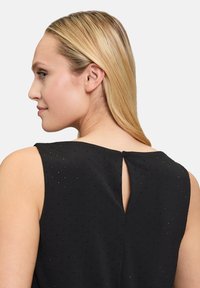 Schwarzes ärmelloses Oberteil mit kleinem Punktemuster, ausgestattet mit einem Schlüssellochverschluss am Rücken und einer glatten Stofftextur.