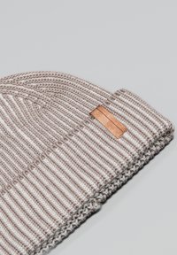 Cappello a maglia color marrone chiaro con strisce bianche, caratterizzato da un motivo testurizzato e una piccola etichetta in tessuto marrone sul lato.