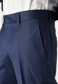 Navy blue trousers made of textured fabric; features a flat front and side pockets, with a tailored waistband for a fitted silhouette.