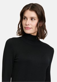 Schwarzer Rollkragenpullover aus weichem Material, mit langen Ärmeln und tailliertem Schnitt. Glatte Textur, keine Muster oder zusätzlichen Akzente.