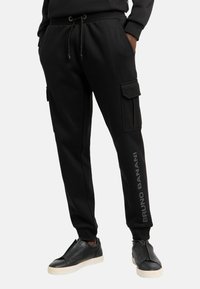 Zwarte joggingsbroek van zachte stof, met een trekkoord in de taille, zijzakken en een logo-detail op het linkerbeen.