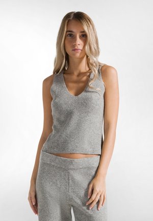 Lichtgrijze, geribbelde gebreide tanktop met een V-hals en mouwloos ontwerp. Zachte textuur met een getailleerde pasvorm. Gecombineerd met bijpassende zachte broek.