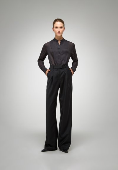 Zwarte button-up shirt in een lichte stof, gecombineerd met hoge, wijde broek. Beide stukken hebben een slanke, op maat gemaakte uitstraling.