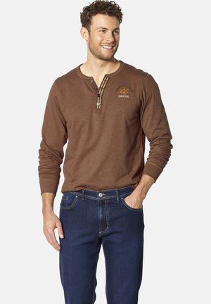 Brown long-sleeve shirt with a Henley neckline, featuring contrasting buttons and a small embroidered logo. Paired with blue denim jeans.