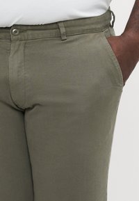 Pantalones de color verde oliva hechos de una mezcla de algodón, con un cierre de botón único, trabillas para el cinturón y bolsillos laterales con una textura suave.
