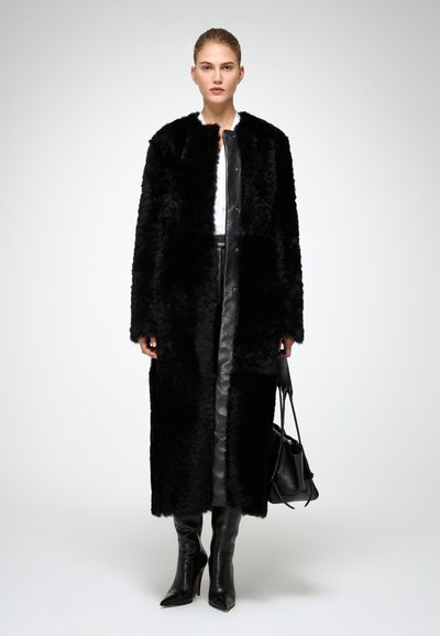 Cappotto lungo in finta pelliccia nera con frontale in pelle liscia, maniche texture e chiusura a bottone. Abbinato a stivali neri in pelle al ginocchio.
