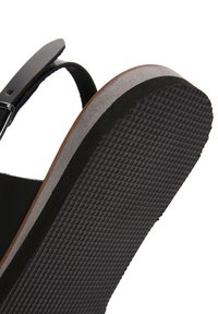 Sandalia negra con una correa ajustable, suela texturizada gris y borde marrón suave. Presenta una base de goma para mayor tracción.