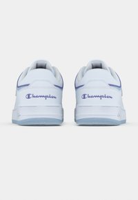 Λευκά sneakers χαμηλού τύπου με λογότυπο "Champion" σε ανοιχτό μωβ στο τακούνι και σόλα σε ανοιχτό μπλε, με θέα από πίσω σε λευκό φόντο.