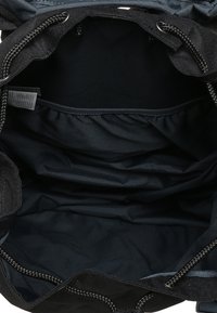 Svart canvasväska med en strukturerad yta, med en bred öppning och dragsko-stängning och ett rymligt, fodrat inre.