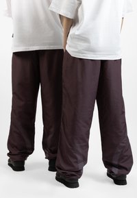 Loose-fitting, dark maroon athletic pants with a smooth texture, mesh accents, and elastic cuffs, paired with white T-shirts.