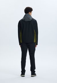 Giacca nera con felpa grigia e accenti verdi sui lati, abbinata a pantaloni e scarpe neri. Tessuto morbido, design funzionale e vestibilità atletica.