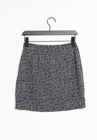 Jupe noire avec un motif tacheté blanc, fabriquée en tissu léger, avec une taille froncée et un ourlet légèrement courbé. Accrochée à un cintre noir.