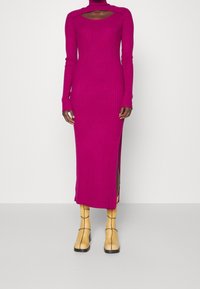 Robe en maille côtelée fuchsia à manches longues, col en U et fente latérale, associée à des bottes à talons blocs jaunes.