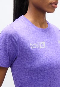 Μωβ αθλητική μπλούζα με υφασμάτινη υφή, στρογγυλό ντεκολτέ και λευκό τυπωμένο λογότυπο στο στήθος.