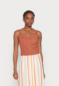 Top cropped de cor ferrugem com decote coração, botões à frente e alças finas; combinado com uma saia de riscas multicoloridas.