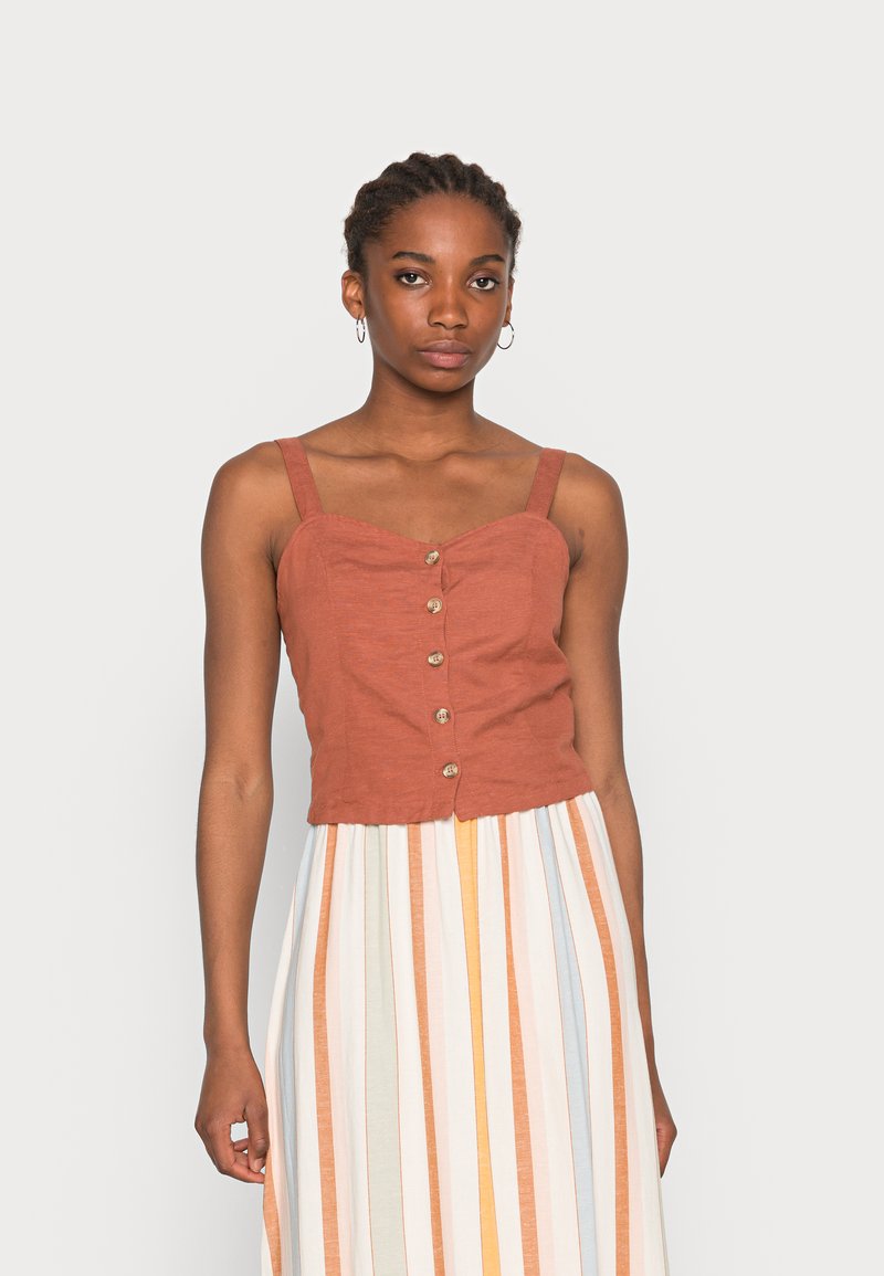 Top cropped de cor ferrugem com decote coração, botões à frente e alças finas; combinado com uma saia de riscas multicoloridas.
