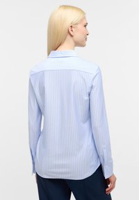 Lichtblauw gestreept blouse, lange mouwen, spitse kraag en knoopmanchetten. Glad stof met verticale strepen en een licht gebogen zoom.
