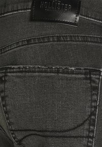 Närbild av svarta denimjeans bakficka med synlig söm och en svart läderetikett från Hollister-märket ovanför.