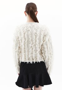 Maglione crema con frange, superficie testurizzata, scollo rotondo e maniche lunghe, abbinato a una gonna a campana nera con righe sottili.