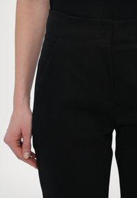 Zwarte op maat gemaakte broek met een gladde textuur, hoge taille en plooien aan de voorkant. Heeft een slanke silhouet en subtiele stikseldetails.