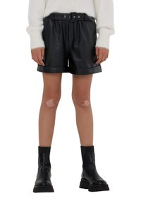 Pantaloni corti neri in pelle con vita regolabile, risvolti e una texture liscia. Abbinati a stivali neri alla caviglia per un contrasto.