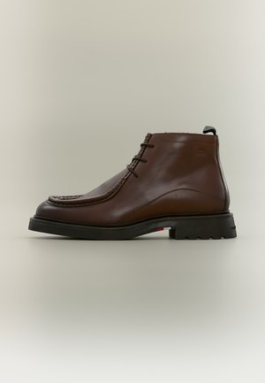 Bottine en cuir marron avec semelle noire, lacets à l'avant et languette à l'arrière, présentée sur un fond neutre.