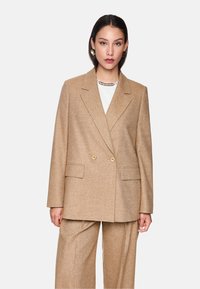 Beige Doppelreiher-Blazer aus strukturiertem Stoff, mit Schößchen, zwei vorderen Taschen und goldfarbenen Knöpfen.