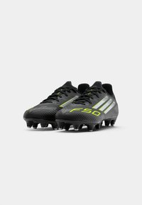 Schwarze Fußballschuhe mit einer strukturierten Oberfläche, neon-grünen Akzenten und drei weißen Streifen. Mit Stollen für Traktion auf Kunstrasen entworfen.