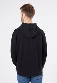 Sweat-shirt à capuche noir en mélange de coton, avec une coupe décontractée, des poignets et un ourlet côtelés, vu de dos avec un jean.