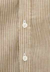 Camicia a righe marrone e bianca con piccoli bottoni bianchi e una consistenza morbida. Vista ravvicinata del tessuto e dei dettagli dei bottoni.