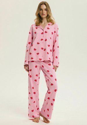 Różowy komplet piżamowy z koszulą na guziki z kołnierzykiem i długimi rękawami oraz dopasowanymi spodniami, oba ozdobione wzorem czerwonych serc.