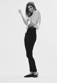 Fehér és fekete csíkos rövid ujjú felső, magas derekú fekete leggingsszel párosítva. A megjelenést fekete balerinacipő teszi teljessé masni részlettel.