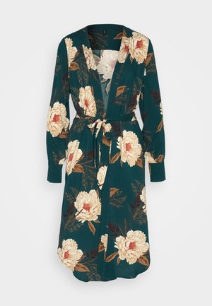 Blomstrande omlotklänning i mörk teal med stora krämfärgade och burgundy blommor. Har långa ärmar, ett knytbälte och en djup V-ringning.