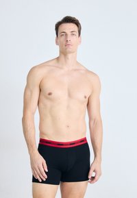 Schwarze Boxershorts mit einem enganliegenden Design und rotem elastischem Bund mit "HUGO"-Branding. Glattes Material mit minimalen Nähten.