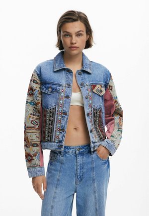Giacca di jeans con pannelli in tessuto a motivi multipli, caratterizzata da colori vivaci e design intricati. Include chiusure con bottoni e due tasche sul petto.