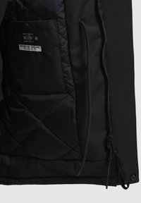 Melnā jaka ar ielāpotu iekšējo oderi, ar rāvējslēdzēja aizdari un plākšņu kabatu. Uz etiķetes rakstīts "KAS TU ARĪ BŪTU".