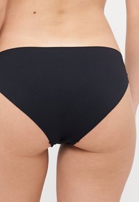 Culotte de bikini noir en tissu lisse. Design taille haute avec une couverture minimale, dotée d'un bord sans couture pour un maximum de confort.