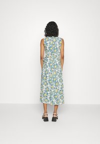 Kukallinen midi-mekko, jossa on valkoinen tausta ja sinisiä sekä keltaisia kukkia, hieman A-linjainen muoto, ilman hihoja ja vyötärölle solmittava yksityiskohta.